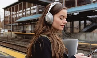 Kvinde med støjreducerende hovedtelefoner på en togstation