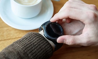 Person tjekker smartwatch og drikker kaffe