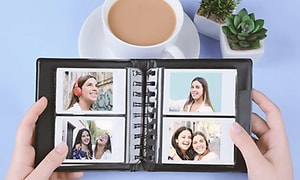 person, der holder et fotoalbum med fire fotos over et blåt bord med kaffe og en grøn plante