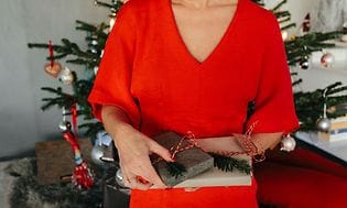 Kvinde i rød kjole med julegaver i hånden foran et juletræ