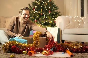 Billede af mand i færd med at pakke gaver ind foran juletræ