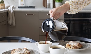 Kvinde hælder kaffe i kopper fra kaffekande
