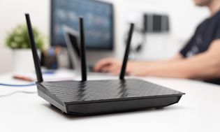 Router på et skrivebord og en mand, der skriver på en computer i baggrunden