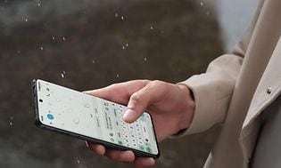Telecom - OnePlus - OnePlus 12 - En person, der skriver på sin OnePlus 12 i regnen