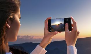 Telecom - OnePlus - OnePlus 12 - En kvinde, der tager et billede af en solnedgang med sin OnePlus 12