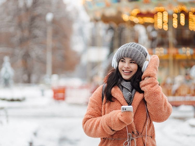 Kvinde med hovedtelefoner og mobil i hånden udenfor på en vinterdag