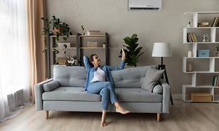 Luftkvalitet - Kvinde i en sofa med fjernbetjening til varmepumpe