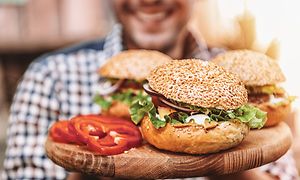 En mand, der holder en tallerken med tre burgere