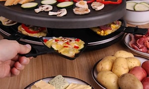 Person der placerer en raclette-pande i en rund raclette med mad
