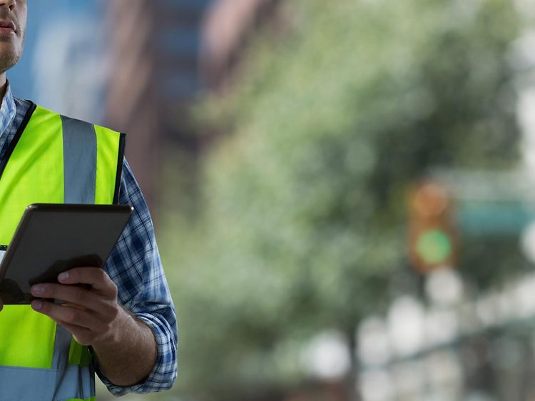Mand med sikkerhedsvest og -hjelm arbejder på tablet udenfor