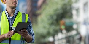 Mand med sikkerhedsvest og -hjelm arbejder på tablet udenfor