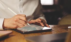 En mand ved et skrivebord bruger stylus med sin tablet