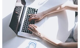 Hænder som arbejder på en laptop på et hvidt bord
