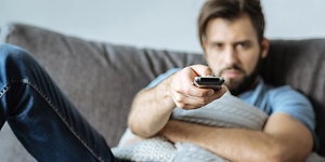 Mand der ser TV i sofaen og peger med fjernbetjeningen