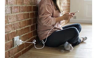 Kvinde der sidder på gulvet med smartphone der oplader