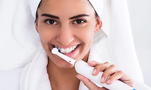 Kvinde der børster tænder med elektrisk tandbørste