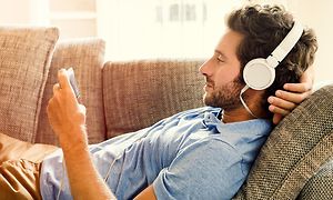 Mand med headset der ligger på sofaen med sin telefon