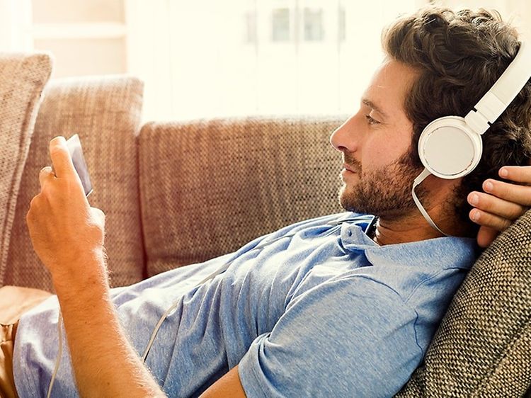Mand med headset der ligger på sofaen med sin telefon