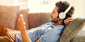Mand med headset der ligger på sofaen med sin telefon