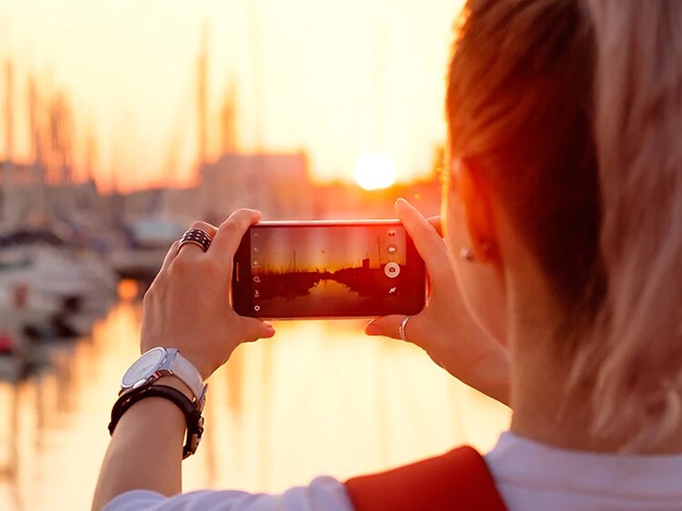 Kvinde der tager billede af en solnedgang ved en havn