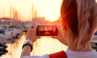 Kvinde der tager billede af en solnedgang ved en havn