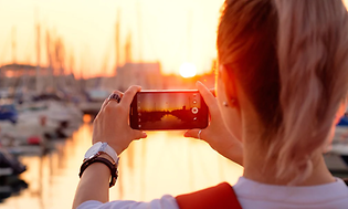 Kvinde der tager billede af en solnedgang ved en havn