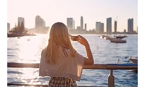 Kvinde der tager et billede af havet med by i baggrunden