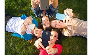 Piger der ligger på græs med deres telefoner i luften