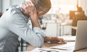 en mand med tydelig ondt i nakken arbejder på sin bærbare compute