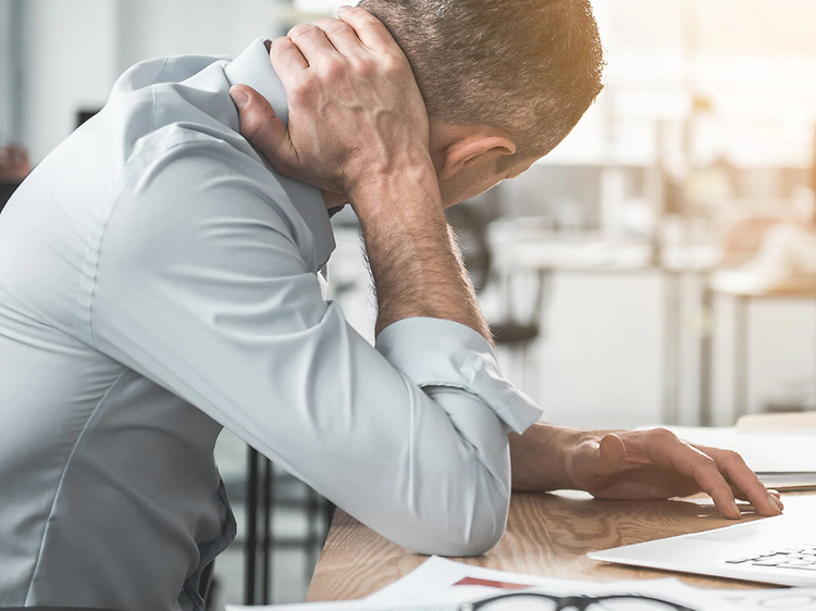 en mand med tydelig ondt i nakken arbejder på sin bærbare compute