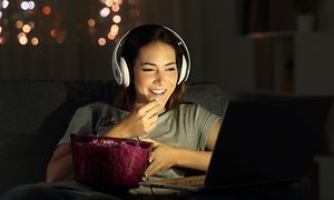 Pige der ser tv, spiser popkorn og har headset på