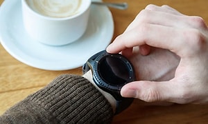 Person der tjekker smartwatch mens han drikker kaffe