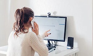 kvinde på sit hjemmekontor snakker i mobil foran computeren