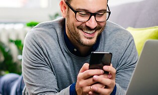 Mand med briller smiler, mens han kigger på sin smartphone
