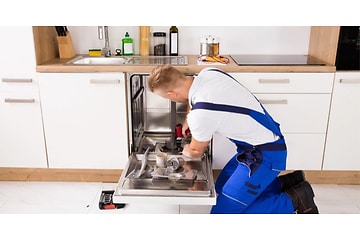Mand i blå overalls installerer en ny opvaskemaskine