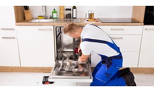 Mand i blå overalls installerer en ny opvaskemaskine