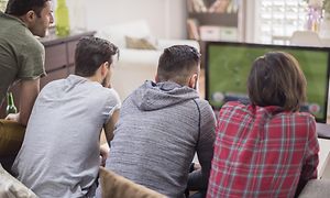 4 mænd i en sofa der ser TV