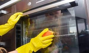 kvinder der rengører sin ovn udvendigt med gule handsker på
