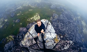 Mand med en selfiestick på en klippe i havet