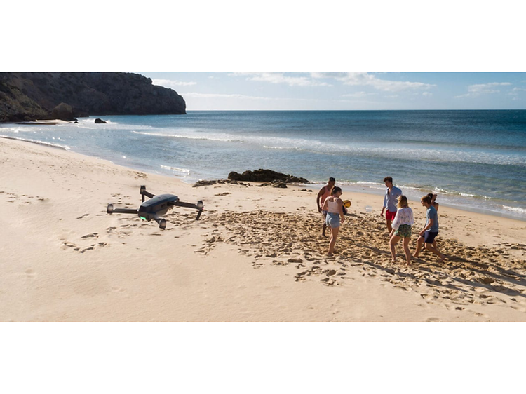 Venner samlet på strand med drone