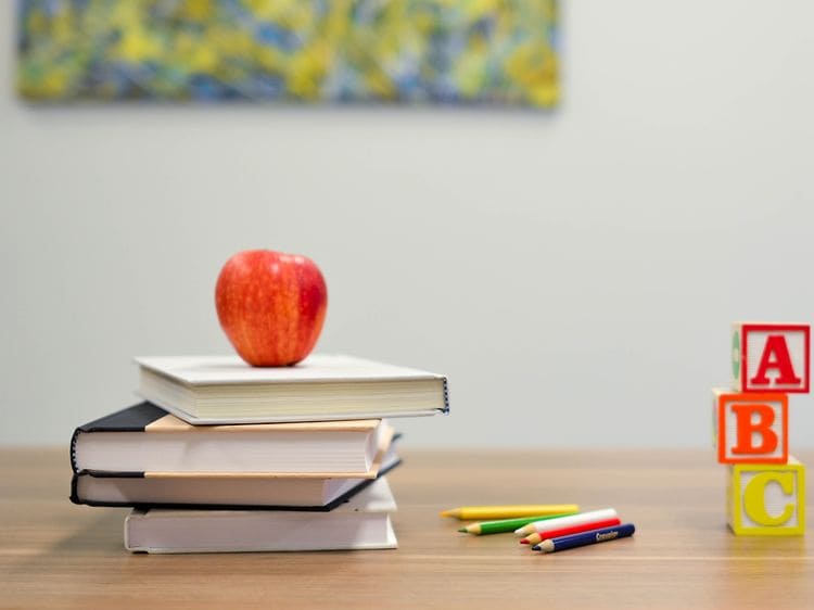 En stak bøger med et æble oven på, samt farveblyanter og klodser på et bord