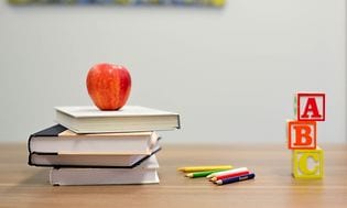 En stak bøger med et æble oven på, samt farveblyanter og klodser på et bord