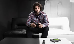 Mand der holder et joystick med Nvidia Shield og fjernbetjening der ligger på et hvidt bord